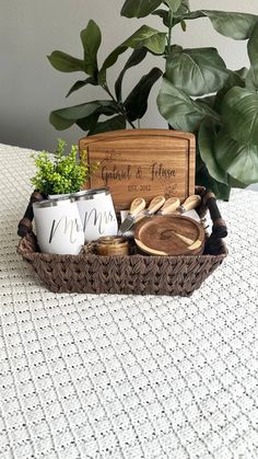 a basket with coffee mugs and other items in it on a table next to a potted plant