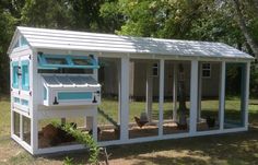 a small white chicken coop with windows and doors on the side, in front of some trees