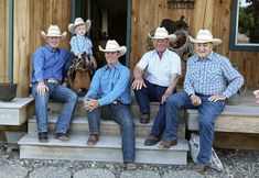 four men in cowboy hats sitting on steps with one man holding a small child and the other standing