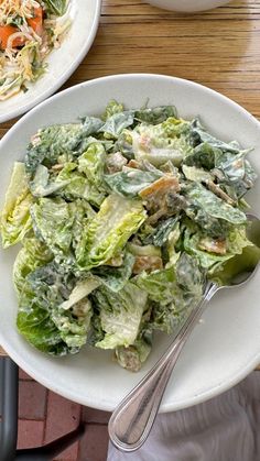 two white plates filled with salad on top of a wooden table next to silverware