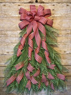 a red and white christmas tree made out of green leaves on a wooden surface with a bow