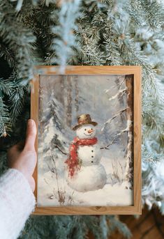 a person holding up a snowman ornament in front of a christmas tree