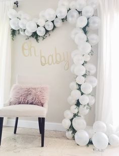 a chair sitting in front of a white balloon arch with the words oh baby on it