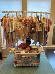 an open trunk sitting on top of a blue rug next to a shelf filled with baby clothes