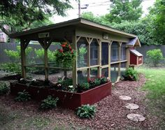 a chicken coop in the middle of a yard with flowers growing on it's roof