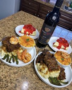 four plates with different types of food on them and a bottle of wine in the background