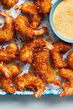 a tray filled with shrimp next to a bowl of dipping sauce and lime wedges