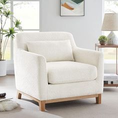 a white chair sitting in a living room next to a lamp and painting on the wall