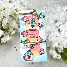 a card with birds and a birdhouse on it next to some white flowers in the background