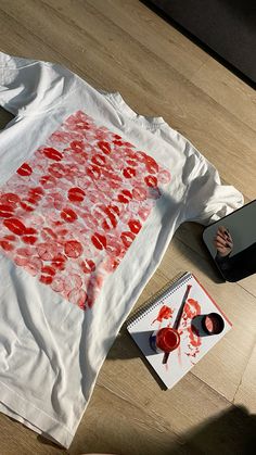 a person sitting on the floor using a laptop computer and drawing with red ink onto a t - shirt