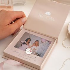 a person holding a necklace in front of a box with a photo on it and a pink ribbon