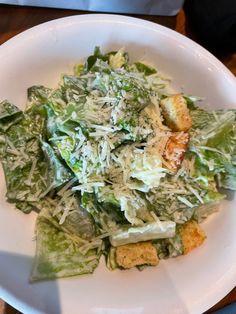 a white plate topped with lettuce and croutons on top of a wooden table