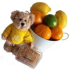 a teddy bear wearing a yellow sweater next to oranges and lemons in a bucket