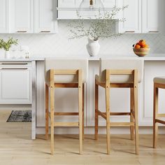 two wooden stools sitting in front of a white kitchen island with fruit on it