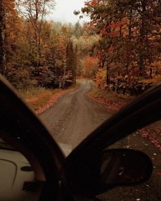 a car driving down a dirt road in the middle of fall trees and foliage on both sides of the road