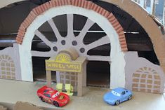 two toy cars are parked in front of a wheel well sign and some cardboard boxes