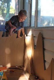 a young boy sitting on top of a cardboard box in front of a windowsill