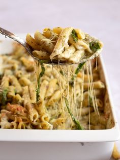 a spoon full of pasta being lifted from a casserole dish with chicken and spinach