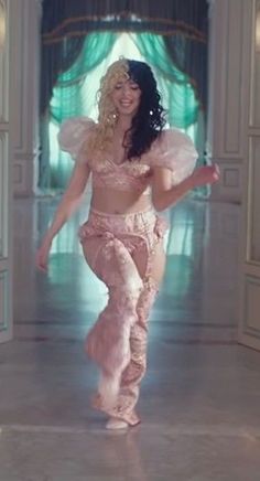 a woman dressed in pink is walking down the hall with her arms out and legs spread wide