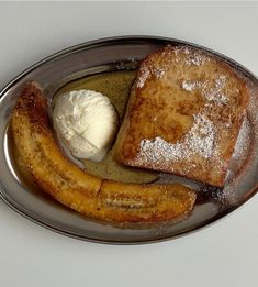 french toast, banana and ice cream on a plate with silver rimmed serving dish