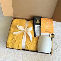 an open box containing a yellow blanket, mouse and coffee mug with the contents in it