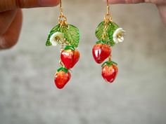 a pair of strawberry earrings with green leaves and red berries hanging from gold - plated earwires