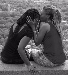 two women are sitting on the edge of a ledge and one is kissing the other