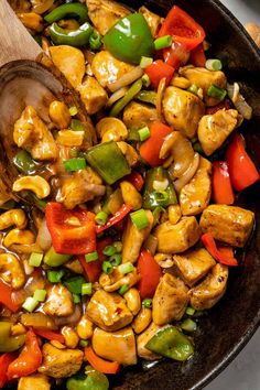 a skillet filled with chicken, bell peppers, and green peppers next to a wooden spoon