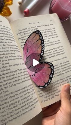 someone is holding an open book with two butterflies on it and the pages are pink