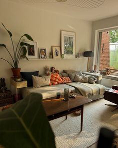 a living room filled with furniture next to a window covered in plants and framed pictures