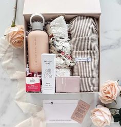 an open box containing the contents of a personal care gift set and flowers on a marble surface