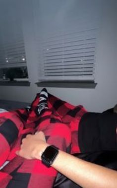 a man laying in bed with an apple watch on his arm and wearing a red checkered shirt