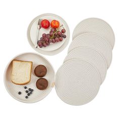 a white plate topped with bread and grapes next to other plates filled with food on top of it