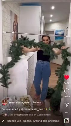 a woman standing in front of a kitchen counter next to a christmas wreath on top of a refrigerator