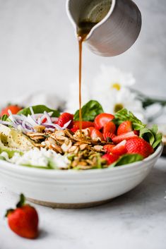 someone pouring dressing over a salad with strawberries