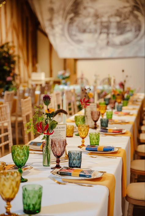 Tablescape using multi-coloured goblets and tumblers, gold napkins and whimsical floral displays in mismatched vases. #Wedding #Tablescape #Colorful #Gold #Barn #Summer #Design #WeddingStyle 📸 Zara Davis Coloured Glassware Table Settings, Mismatched Table Setting Mix Match, Wedding Table Glasses, Colorful Wedding Plates, Coloured Glassware Wedding, Multicolored Glassware Wedding, Mismatched Cups Wedding, Mismatched Plates Dinner Party, Assorted Glassware Wedding