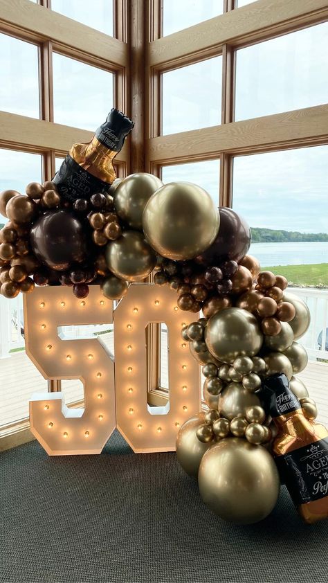 A chrome gold, brown and copper balloon garland with whiskey bottle mylar balloon accents drape over a lit up number 50 marquee for a milestone birthday celebration. 50th House Party Ideas, Whiskey Theme Party Decor, Mens Birthday Set Up, Balloons For Men Birthday, Birthday Decorations 50th Man, Aged To Perfection Balloon Garland, 50tj Birthday Party Ideas For Men, Aged To Perfection Balloons, Balloon Decorations 50th Birthday