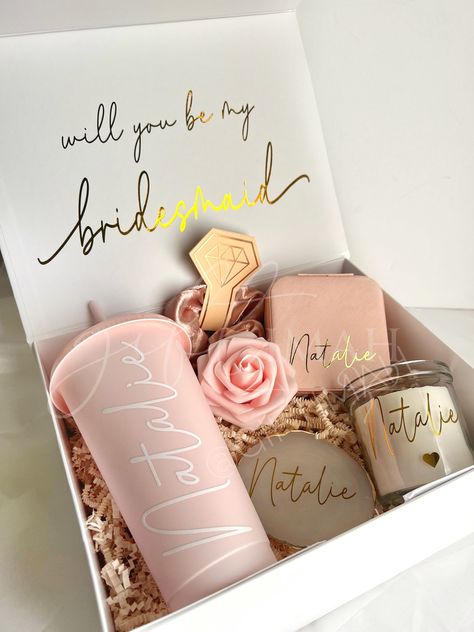 These beautiful pink and gold themed deep large filled boxes make the perfect gift for your bride tribe, packed with an excellent variety of personalised goods these are sure to make the best surprise! Value works out much better than purchasing each item individually! Details: EVERY ORDER COMES WITH: -White magnetic box: 11"x8"x4" Personalised with gold name and inside message. Comes with ivory crinkled paper inside. Tied with pink frayed ribbon. -Pink foam rose ITEMS INCLUDED IN BOX WILL VARY Bride Made Gifts Ideas, Cute Gifts For Bridesmaids, Bridesmaid Proposal Box Ideas Purple, Gifts For Bridesmaids From Bride, Bridesmaid Hamper Ideas, Wedding Gift Packing, Gift Packing Ideas, Bride Theme, Crinkled Paper