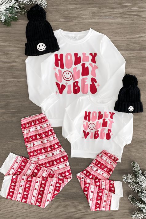 *Adult & child sets sold separately* Pajama set features a white long sleeve top and pair of Nordic print pants Mom & child sets both feature a "Holly Jolly Vibes" design Soft fabric provides cozy all-night comfort Perfect for bedtime or a Christmas movie marathon Gift you and your little ones' wardrobe a seasonally sweet vibe with these "Holly Jolly Vibes" Pajama Sets. These pajama sets come with a long sleeve top and pair of matching bottoms. Both pieces are made from a soft fabric blend for c Matching Sister Christmas Outfits, Christmas Pajamas Outfit, Christmas Pajamas Photoshoot, Couples Christmas Pajamas, Christmas Movie Marathon, Kids Christmas Shirts, Fabric Outfits, Cozy Christmas Outfit, Family Matching Christmas Pajamas