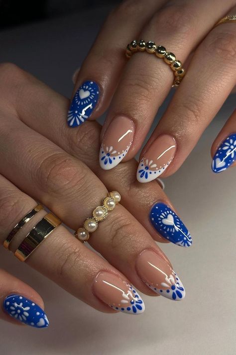 These almond-shaped nails are a playful mix of summer vibes with a contrasting design. The vibrant blue base pops with white floral patterns and heart shapes, while the clear nails are elegantly simple with a hint of white floral art and subtle line accents. The pairing of bold and subdued creates a lovely and engaging aesthetic perfect for sunny days.  // Photo Credit: Instagram @chibimoon.nails Nail Design Clear Base, Simple Blue Heart Nails, Blue Nails For Short Nails, Fake Nail Design Ideas, Oval Shaped Summer Nails, Vacation Nails Blue And White, White French With Blue Design, French Tip With Accent Nail Design, Short Almond Nails Elegant