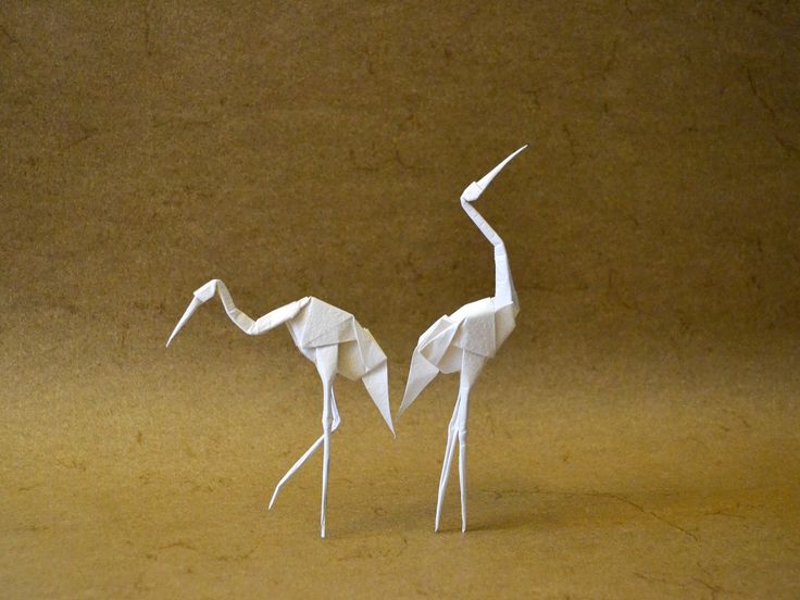 two white origami cranes standing next to each other on a brown surface,