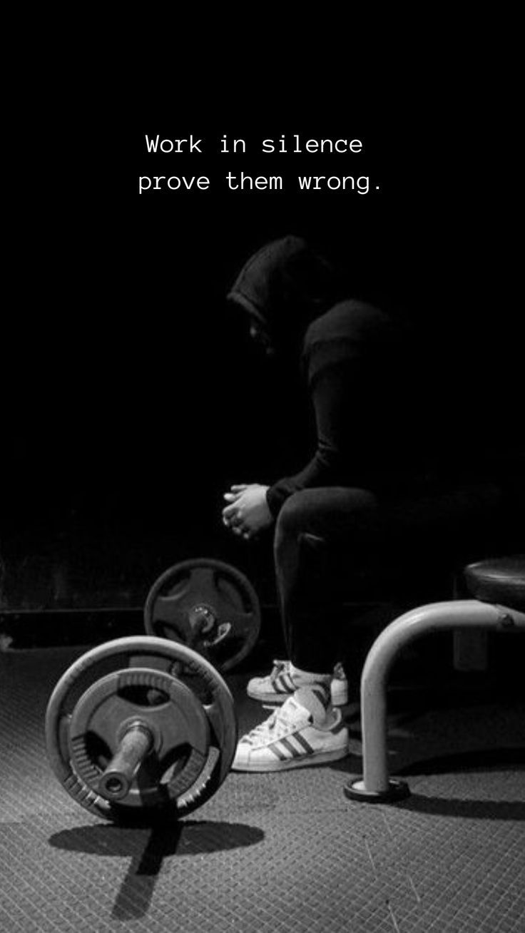 a man squats on the ground with a barbell in front of him and an exercise wheel behind him