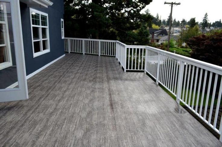 a wooden deck with white railings next to a blue wall and trees in the background