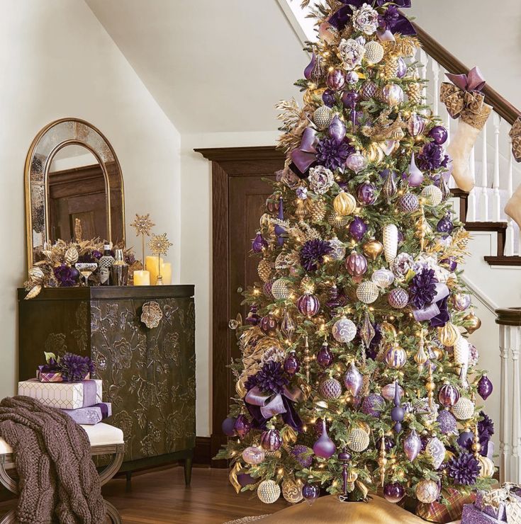 a decorated christmas tree with purple and gold ornaments in a living room next to stairs