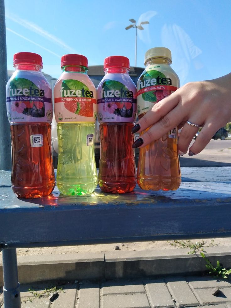 three bottles of juice sitting on top of a blue table next to a person's hand