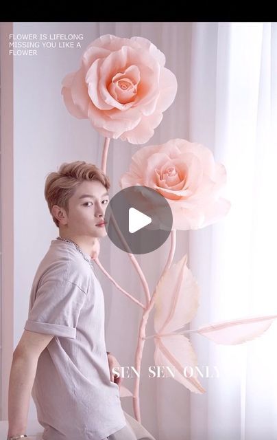 a young man sitting next to a pink flower