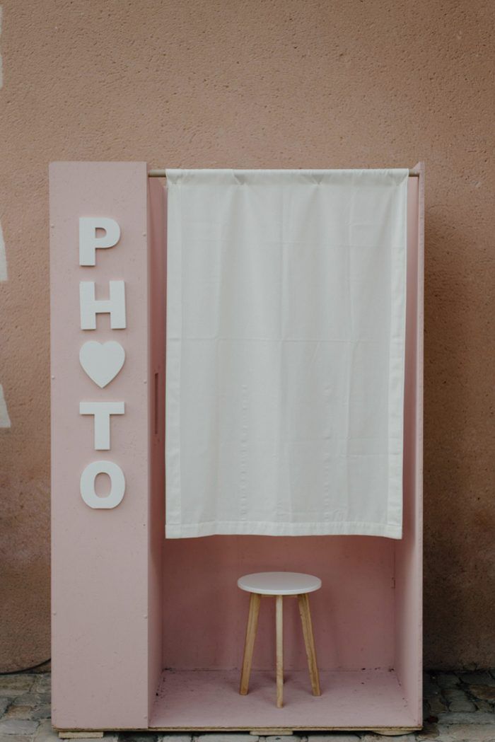 a pink photo booth with a white curtain on it's side and a stool in front