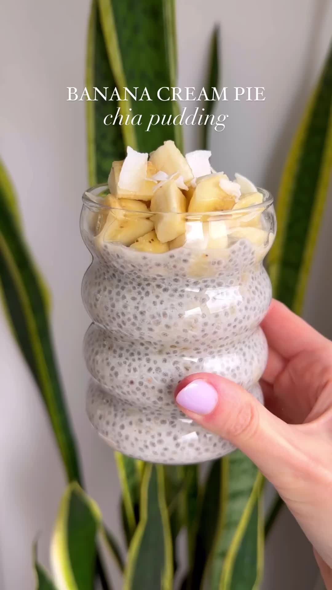 This may contain: a hand holding a small glass bowl filled with chia pudding and pineapple chunks