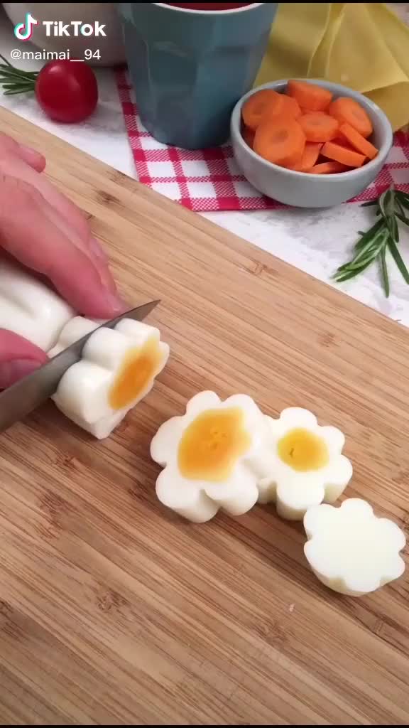 This may contain: someone cutting up boiled eggs with a knife on a cutting board next to some carrots