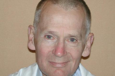 A close-up of a smiling Prof Chris Redman who has closely cropped grey hair and is wearing a white shirt.